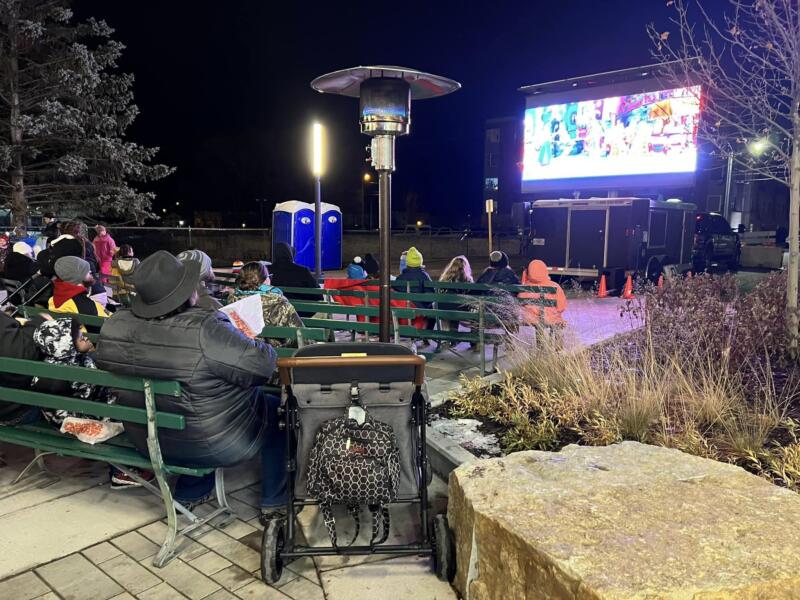 People sitting on benches watching an outdoor movie after dark