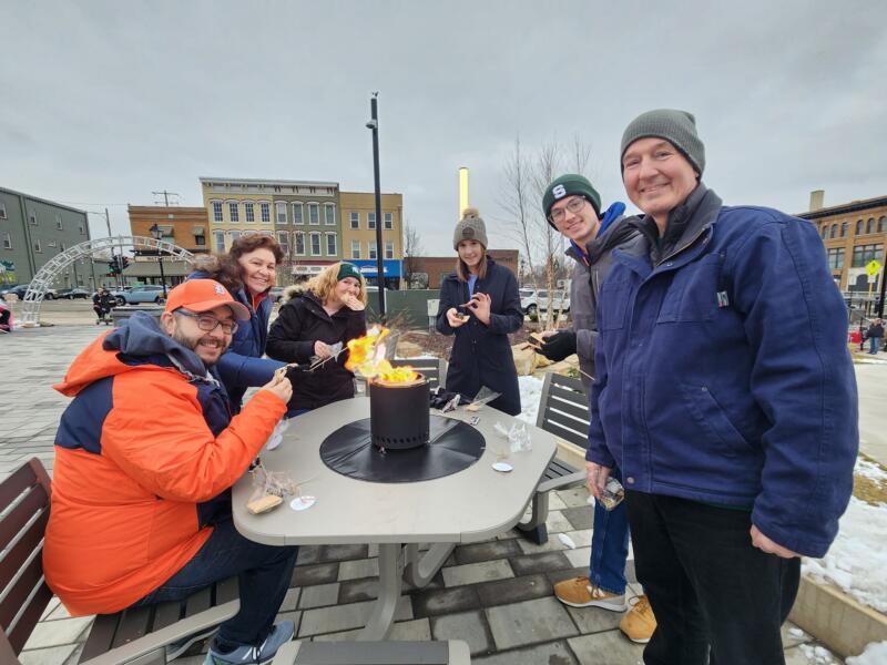 Group of people roasting smores outdoors on a tabletop fire