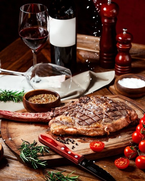 A steak on a cutting board with a wine botte and wine glass, sitting on a table.