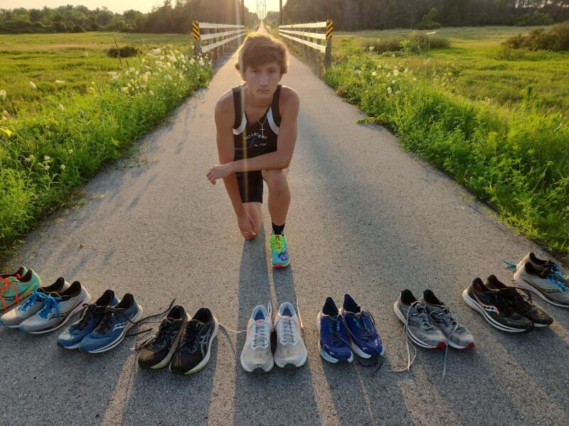 Boy with multiple pairs of running shoes in front of him, posing on the Interurban Trail in Watertown Wi