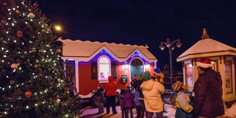 A Christmas tree, red santa house, and kiosk with a line of kids to see Santa