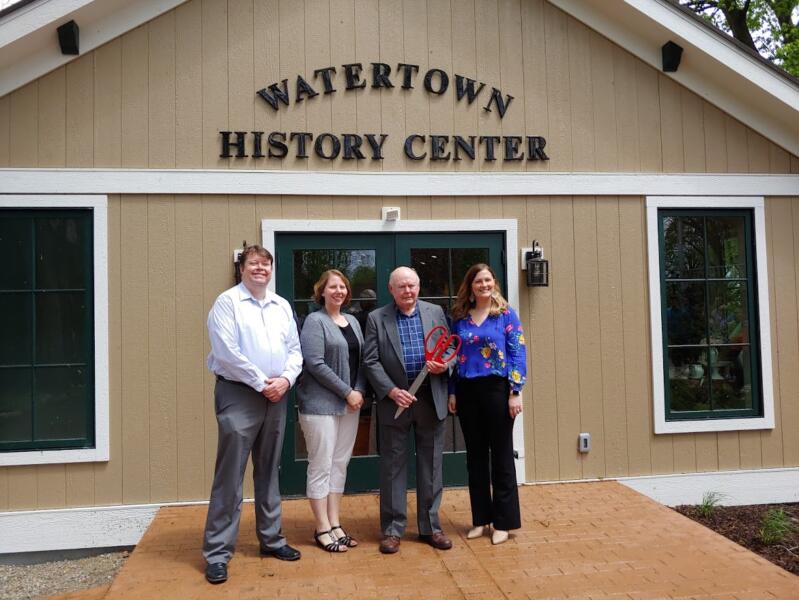 four people standing outside of the Watertown History Center, posing for its ribbon cutting