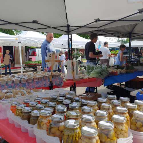 Jars on a table at a farmers market with people shopping the booth.