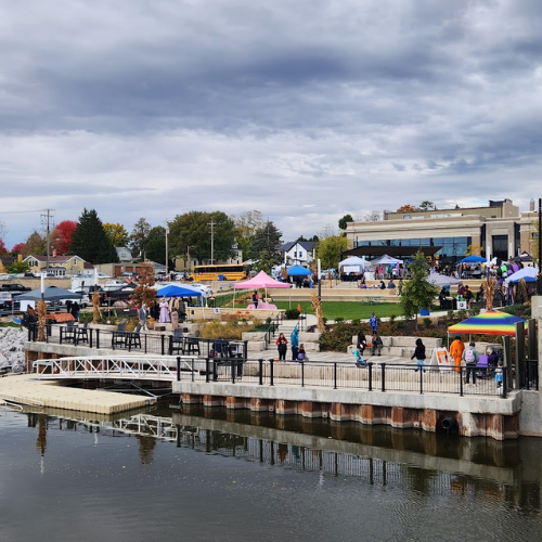 Tents and a crowd at a river-side park in downtown Watertown.