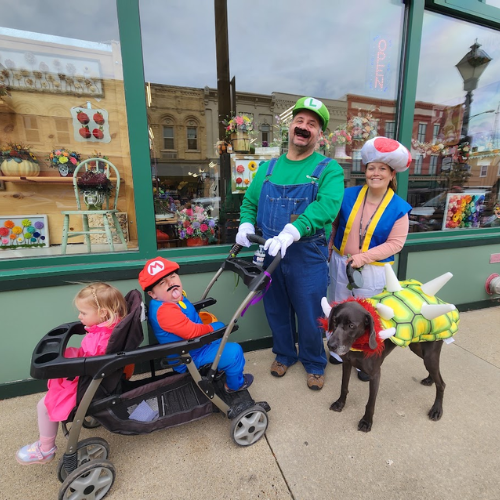Family dressed in Halloween costumes, pushing a stroller and walking a dog